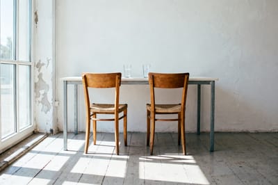 Zwei leere Holzstühle an einem hellen, völlig leeren Tisch mit zwei Wassergläsern
